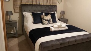 Uma cama bem arrumada com cabeceira escura, lençóis brancos e um travesseiro decorativo.