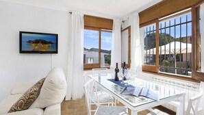 Una habitación moderna con una mesa de vidrio, muebles blancos y un televisor que muestra una vista panorámica.