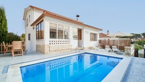 Zona junto a la piscina con piscina, sillas de madera y un edificio de fachada de piedra y tejado de tejas.