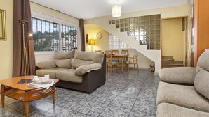 Un salon comprenant un canapé, une table basse et un coin repas avec des chaises et une table. Un escalier mène à un autre niveau.