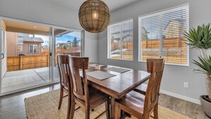 Un comedor con mesa y sillas de madera, una lámpara colgante de fibras tejidas y ventanas amplias con persianas.