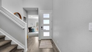 Un interior moderno con una escalera, una puerta con paneles de vidrio esmerilado y un pasillo que conduce a una habitación con escritorio y silla.