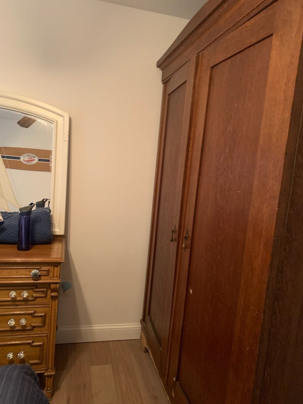 A bedroom with a wooden wardrobe, a dresser with drawers, and a mirror with a decorative frame.