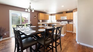 A spacious kitchen with wooden cabinets, a dining table with chairs, and a large window. - The Broadmoor House (Pasco)