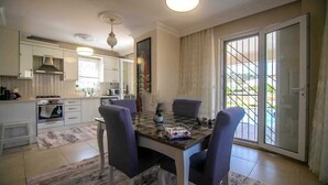 A modern kitchen with white cabinets, a built-in oven, and a dining area with a glass table and four chairs. - Inviting 4-Bed Villa Nil Dalyan with child pool (Ortaca)