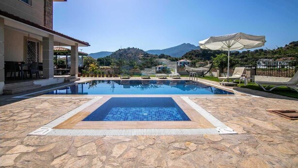 A swimming pool with a stone deck, lounge chairs, and umbrellas. - Inviting 4-Bed Villa Nil Dalyan with child pool (Ortaca)