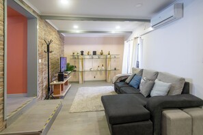 A living room with a sofa, a coffee table, a TV, and a glass shelf with decorative items. - Chapel House (Ponta Delgada)