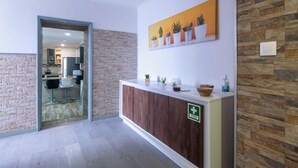 Un espace d’accueil avec un comptoir en bois, un panneau vert indiquant la sortie de secours et une présentation de plantes en pot.