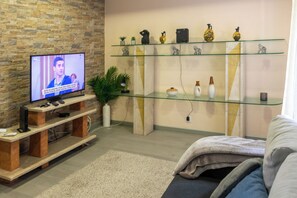 A living room with a TV, wooden entertainment unit, glass shelves with decorative items, and a sofa. - Chapel House (Ponta Delgada)