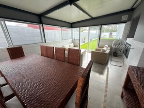 A covered outdoor dining area with a table and chairs, a sofa, and a grill. - Chapel House (Ponta Delgada)