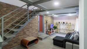 Un salon moderne avec un mur en pierre, un escalier, un téléviseur à écran plat, un canapé et une étagère vitrée.