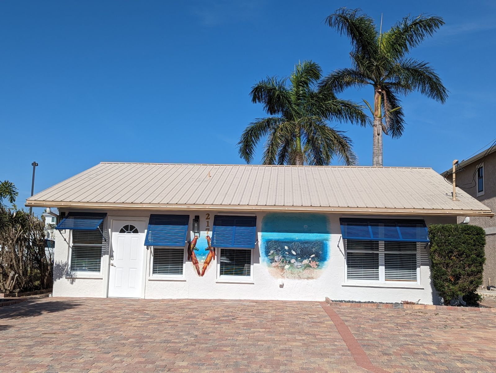 A two-story building with a flat roof, blue shutters, and a brick driveway.