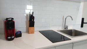 Ett kök med en diskho i rostfritt stål, en svart induktionshäll, ett knivställ och en röd vattenkokare.