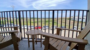 Un balcon avec des meubles en bois, une vue sur les voitures garées et un paysage lointain.