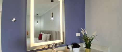 A bathroom with a large mirror, a sink, a towel dispenser, and a potted plant.