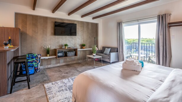 Habitació d'hotel moderna amb un llit gran, una taula de treball amb una cadira, una taula petita, un sofà i un balcó amb vistes.