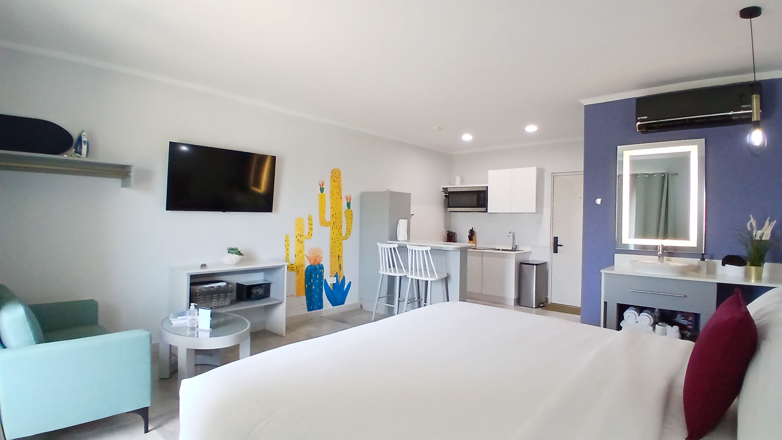Habitación de hotel con cama, escritorio, silla, televisión, microondas, lavabo y espejo.