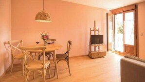 Uma área de refeições com mesa e cadeiras, um lustre e uma televisão sobre um móvel.