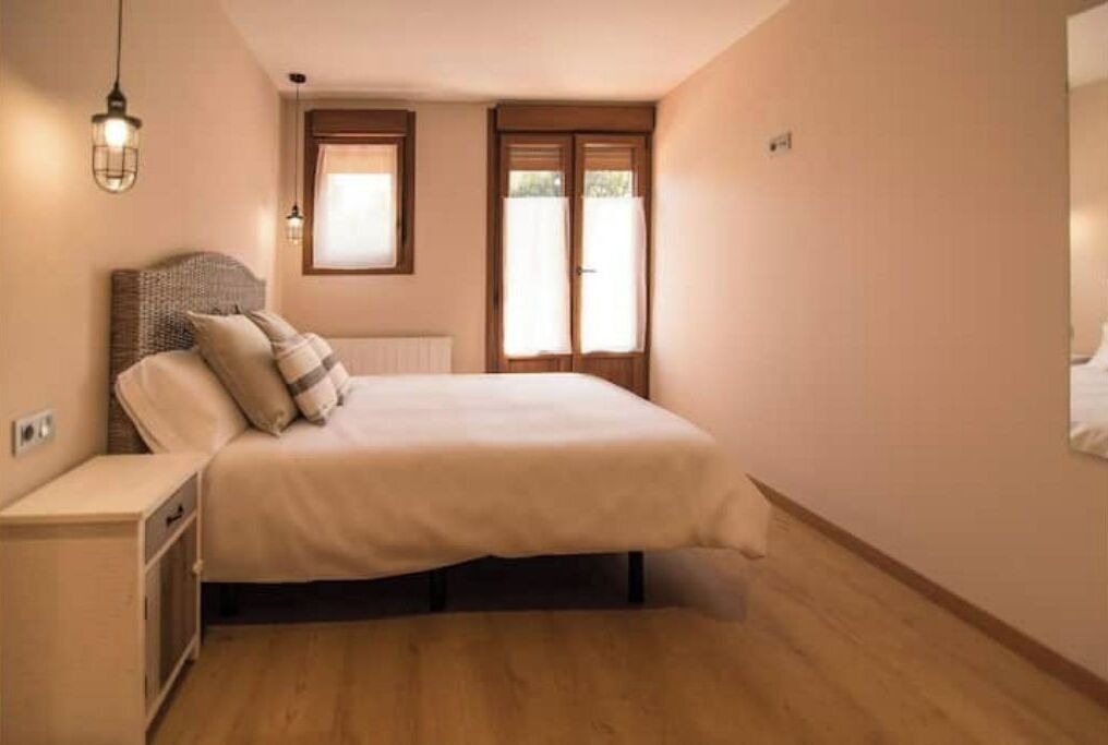 A bedroom with a bed, bedside table, and a window with curtains.
