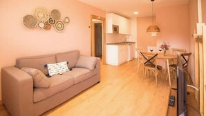 Sala de estar com sofá, mesa de jantar com cadeiras, cozinha e televisão.