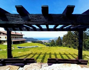 A covered outdoor area with a view of a building and a boat on a grassy field. - Rural Apartment “Balcony with Ocean View” (Munguía)