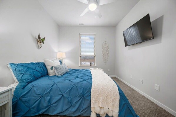 A bedroom with a bed, a ceiling fan, a TV, a window, and a wall-mounted dreamcatcher. - 2BR TC Stay I Near DT + Trails (Traverse City)