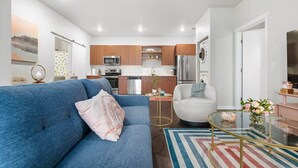 Una sala de estar moderna con un sofá azul, un sillón blanco y una mesa de centro de vidrio.