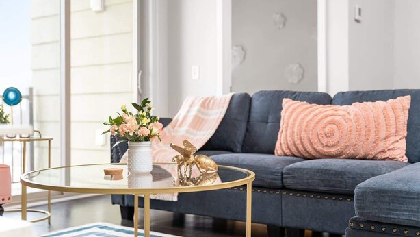 A modern living room with a dark blue sofa, a glass coffee table, and decorative pillows. - Stylish 2BR Suite Near DT Traverse City + Smart TV (Traverse City)
