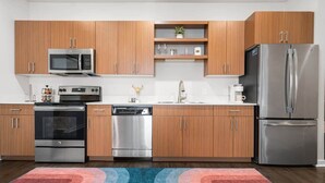 A modern kitchen with wooden cabinets, stainless steel appliances, and a colorful rug. - Stylish 2BR Suite Near DT Traverse City + Smart TV (Traverse City)