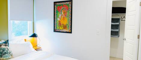 A bedroom with a bed, a window, a framed artwork, and a closet.