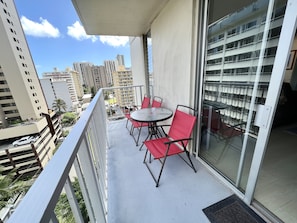 A balcony with a glass door, red chairs, and a small round table.
