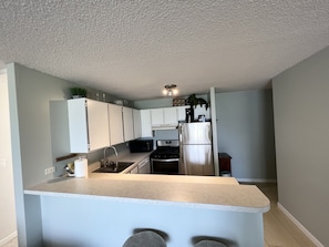 A modern kitchen with white cabinets, a stainless steel refrigerator, a microwave, and a sink.