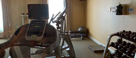 A hotel fitness room with a treadmill, elliptical, and dumbbells.
