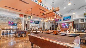 A pool table in a well-lit room with multiple TVs displaying sports events, seating areas, and a wooden ceiling with hanging lights. - Family friendly! Heated pool/free parking/tennis.  (Destin)