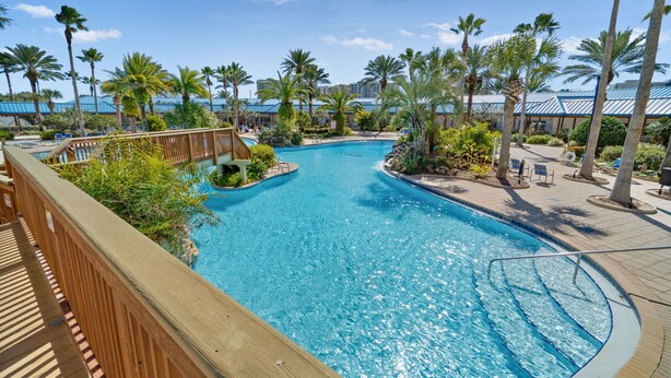 A large outdoor swimming pool surrounded by palm trees and a wooden deck. - Family friendly! Heated pool/free parking/tennis.  (Destin)