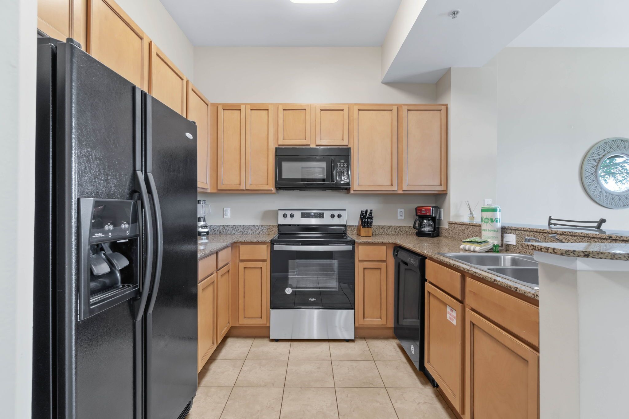A modern kitchen with wooden cabinets, a black refrigerator, a microwave, an oven, and a dishwasher.