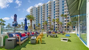 A rooftop lounge with outdoor seating, palm trees, and a view of a tall building. - Family friendly! Heated pool/free parking/tennis.  (Destin)