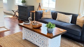 A living room with a dark blue sofa, a wooden coffee table, and a white decorative piece on the wall. - The Kelley House | Suite 2 - 1st floor (Pensacola)