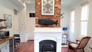 A modern living room with a fireplace, wooden flooring, and a dining area with a table and chairs. - The Kelley House | Suite 2 - 1st floor (Pensacola)