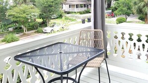 A covered outdoor area with a metal table and wicker chairs, overlooking a residential neighborhood with trees and a house. - The Kelley House | Suite 3 w/Balcony (Pensacola)
