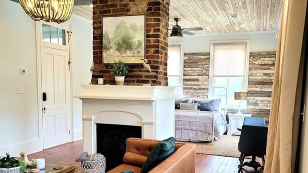 A living room with a fireplace, a brown leather sofa, and a dining area with a table and chairs. - The Kelley House | Suite 3 w/Balcony (Pensacola)