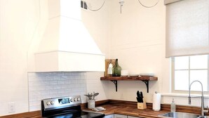 Une cuisine moderne dotée d’une cuisinière en acier inoxydable, de meubles blancs, d’un plan de travail en bois et d’un luminaire suspendu.