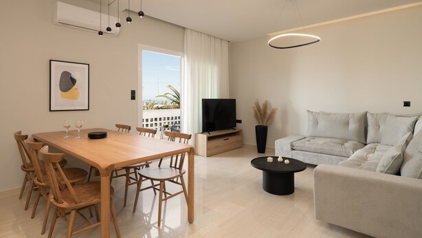 Ein modernes Wohnzimmer mit einem Holzesstisch, einem schwarzen Couchtisch, einem grauen Sofa, einem Flachbildfernseher und einem großen Fenster mit Vorhängen.