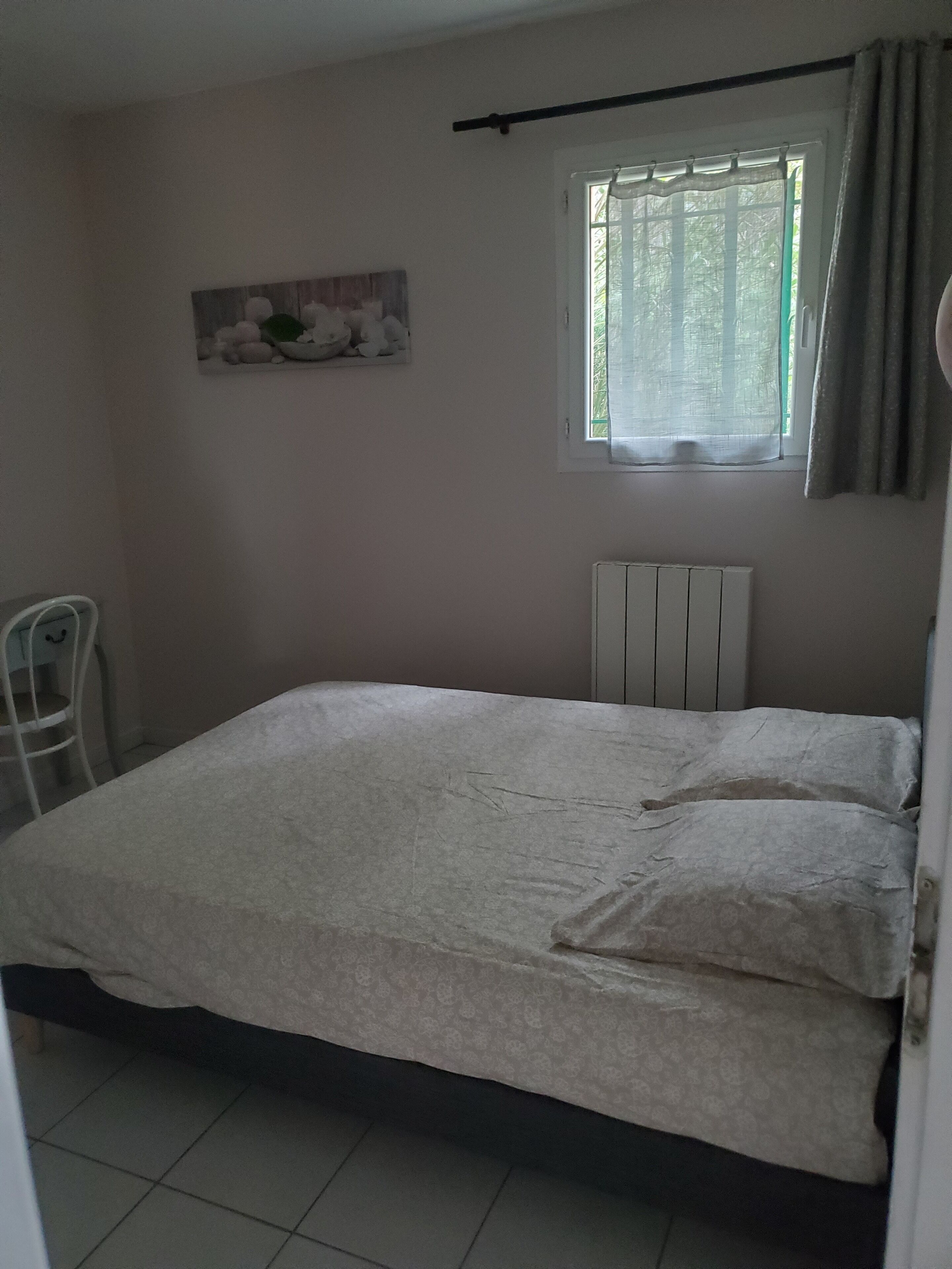 A bedroom with a bed, a radiator, a window with curtains, and a chair.