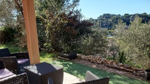 Uma área de pátio ao ar livre com móveis de vime e vista para um jardim bem cuidado e colinas distantes.