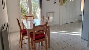 Uma sala de jantar com mesa e cadeiras, um radiador, uma porta e uma janela com cortinas.