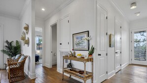 A hallway with wooden flooring, white walls, and a wicker console table with decorative items. - Heated Pool, Steps to Beach, Stylish Interior, Amenities Galore!  (Waveland)