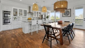 A modern kitchen with white cabinetry, a central island, and two hanging wicker chandeliers. - Heated Pool, Steps to Beach, Stylish Interior, Amenities Galore!  (Waveland)