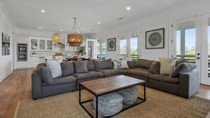 A spacious living room with a sectional sofa, a coffee table, and a kitchen area in the background. - Heated Pool, Steps to Beach, Stylish Interior, Amenities Galore!  (Waveland)