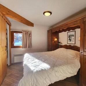 A bedroom with a wooden bed, a window with curtains, a wall-mounted lamp, and a framed picture. - Ski-in/ski-out & foot of the slopes, 3rd floor, swimming pool, sauna, balcony, tv, ski locker, 49m² (Les Orres)